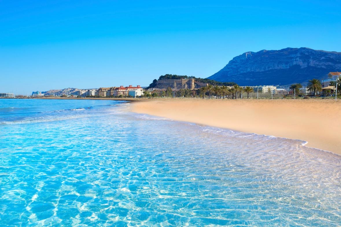 Het strand van Dénia met helder turquoise water en de Montgó op de achtergrond